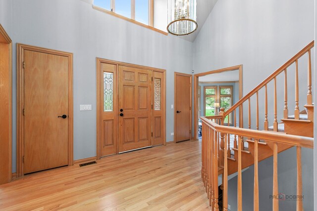foyer with plenty of natural light, a notable chandelier, wood finished floors, and a towering ceiling