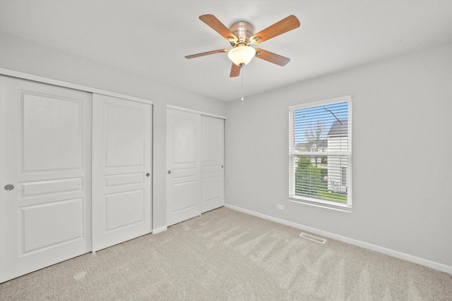 unfurnished bedroom featuring carpet, baseboards, multiple closets, and ceiling fan