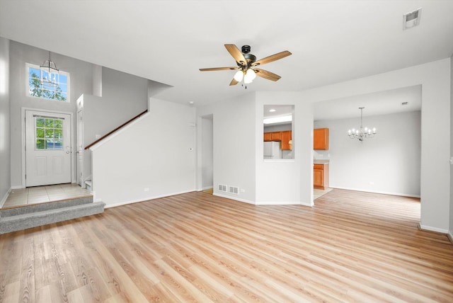 unfurnished living room featuring a chandelier, light wood-type flooring, stairs, baseboards, and a ceiling fan