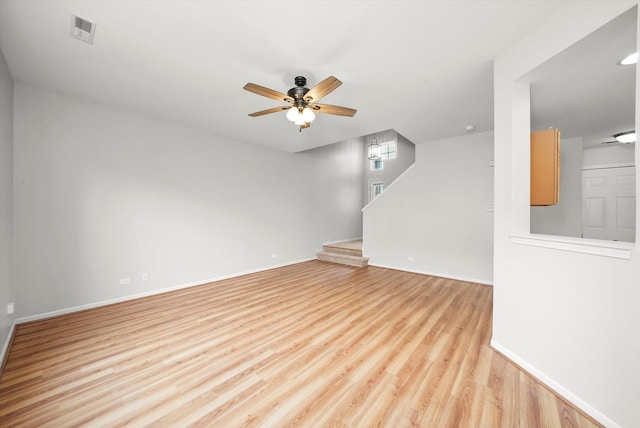 empty room featuring a ceiling fan, light wood-style flooring, baseboards, and stairs