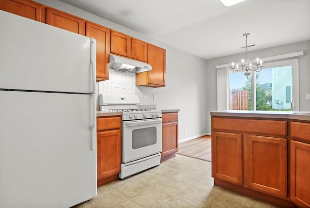 kitchen featuring white appliances, under cabinet range hood, brown cabinets, a chandelier, and pendant lighting