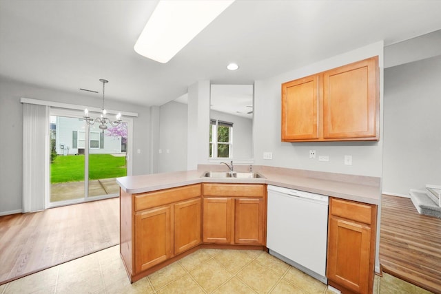 kitchen featuring white dishwasher, a sink, a peninsula, light countertops, and a chandelier