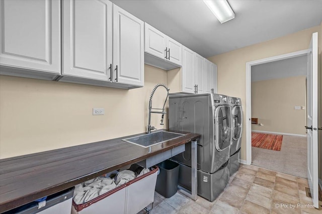 laundry area with cabinet space, a sink, baseboards, light carpet, and washer and dryer