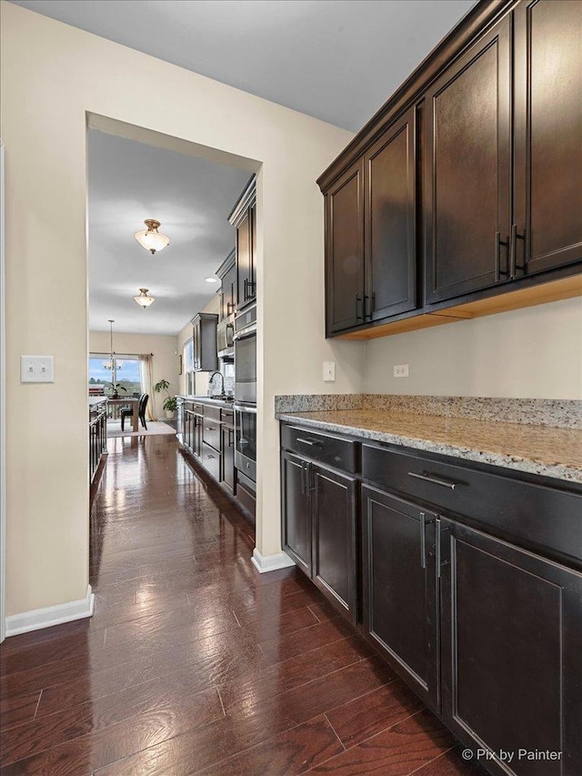 kitchen with baseboards, dark brown cabinetry, dark wood-style floors, and light stone counters
