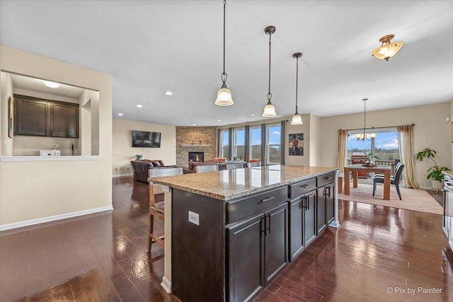 kitchen with a stone fireplace, dark wood finished floors, baseboards, a breakfast bar, and recessed lighting