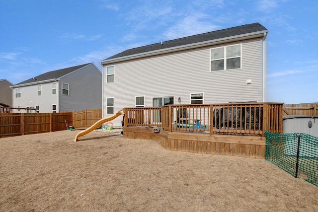 rear view of house with a fenced backyard, a wooden deck, and a playground