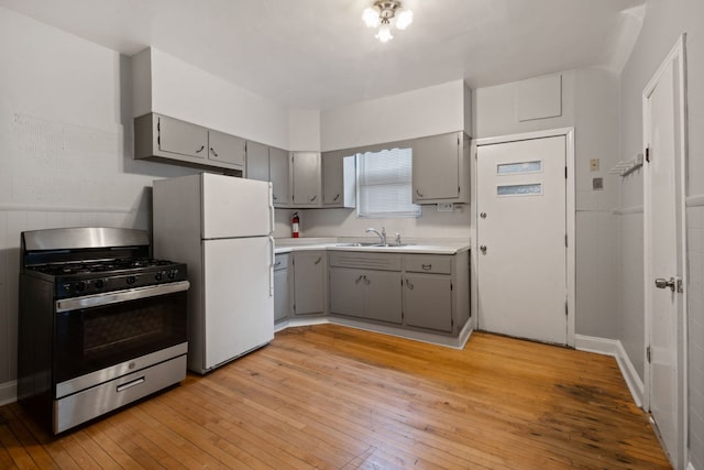 kitchen with stainless steel range with gas stovetop, freestanding refrigerator, light wood-type flooring, a sink, and gray cabinetry