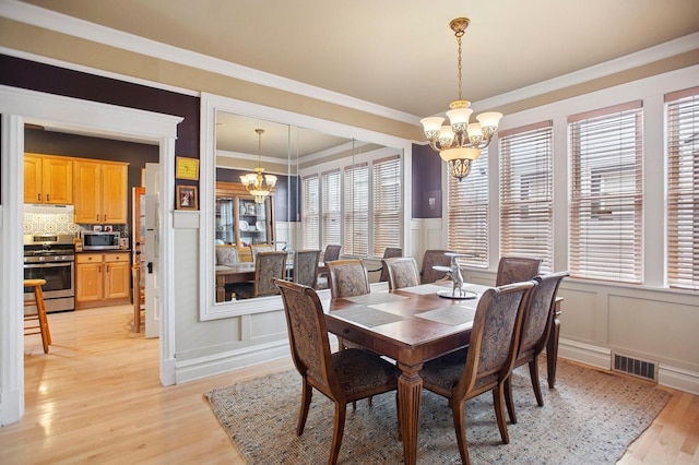 dining area featuring a chandelier, light wood finished floors, visible vents, and a wainscoted wall