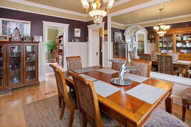dining space featuring a notable chandelier, ornamental molding, wainscoting, arched walkways, and wood-type flooring