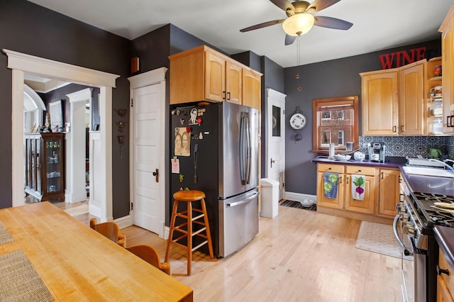 kitchen with baseboards, light wood-style flooring, a ceiling fan, backsplash, and appliances with stainless steel finishes