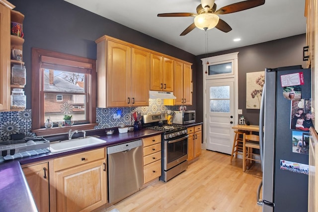 kitchen with a sink, a ceiling fan, dark countertops, under cabinet range hood, and stainless steel appliances