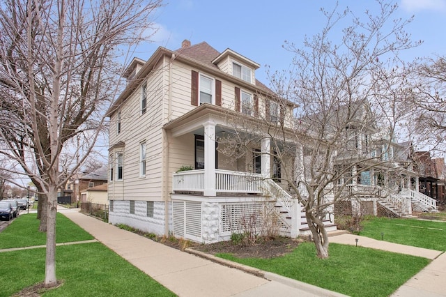 view of front of house featuring a porch, stairs, a front lawn, and a chimney
