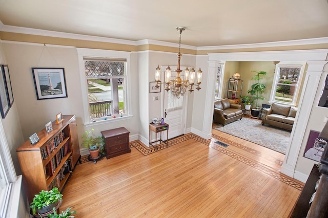 entryway with baseboards, a chandelier, crown molding, light wood-style floors, and visible vents