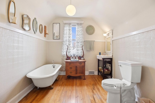 bathroom featuring visible vents, toilet, a soaking tub, hardwood / wood-style floors, and lofted ceiling