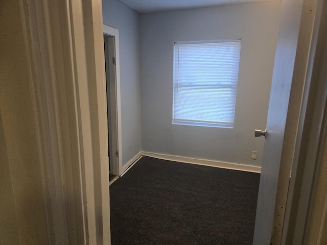 unfurnished room featuring baseboards and dark carpet
