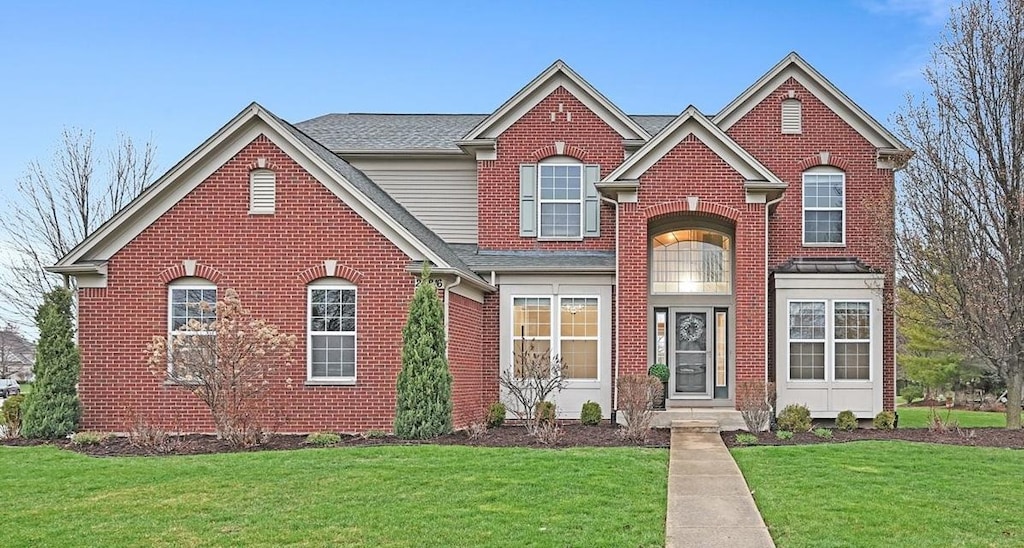 traditional home with roof with shingles, a front lawn, and brick siding