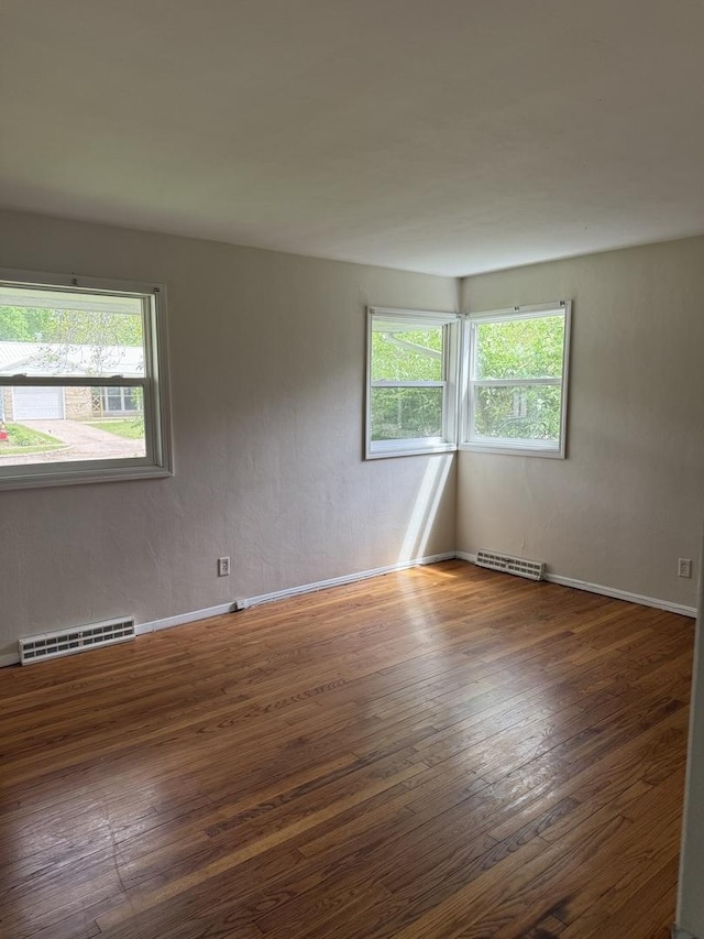 empty room with baseboards, visible vents, and hardwood / wood-style floors