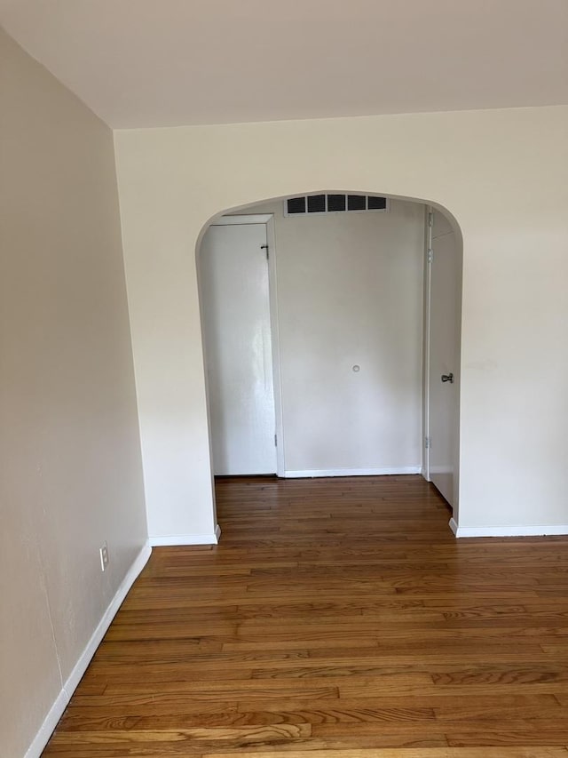 empty room with baseboards, arched walkways, wood finished floors, and visible vents