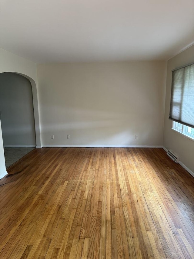 unfurnished room with baseboards, arched walkways, wood finished floors, and visible vents