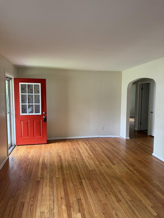 interior space with baseboards, arched walkways, and wood finished floors