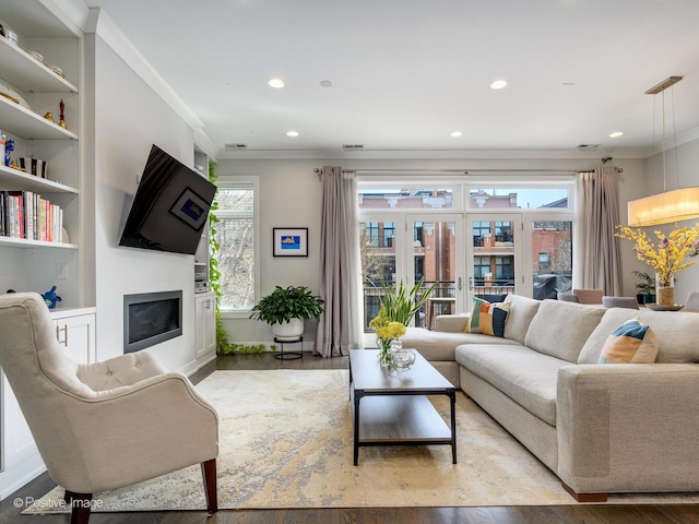 living area with wood finished floors, crown molding, a glass covered fireplace, recessed lighting, and baseboards