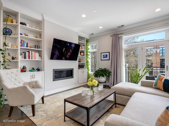 living room featuring ornamental molding, a glass covered fireplace, recessed lighting, built in shelves, and wood finished floors