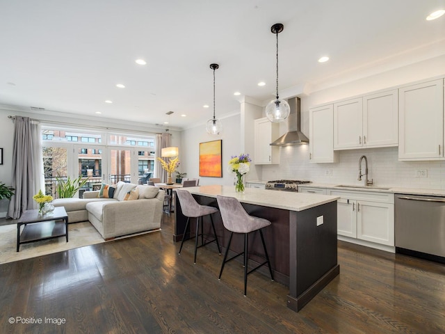 kitchen featuring a sink, appliances with stainless steel finishes, wall chimney range hood, tasteful backsplash, and ornamental molding