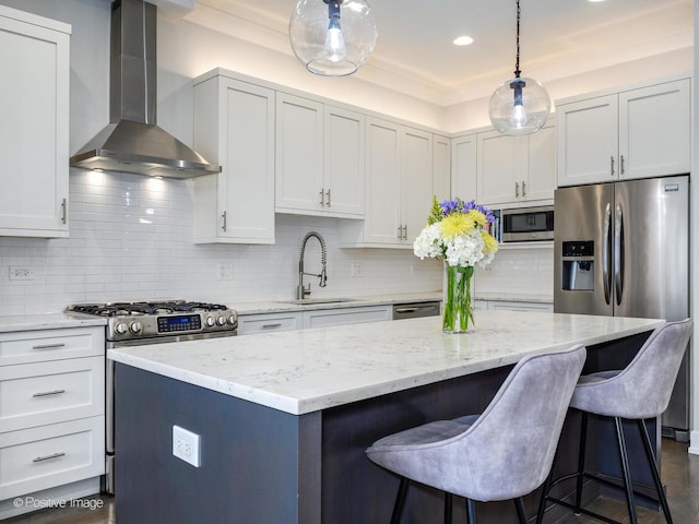 kitchen featuring wall chimney exhaust hood, a sink, appliances with stainless steel finishes, a kitchen island, and a kitchen breakfast bar