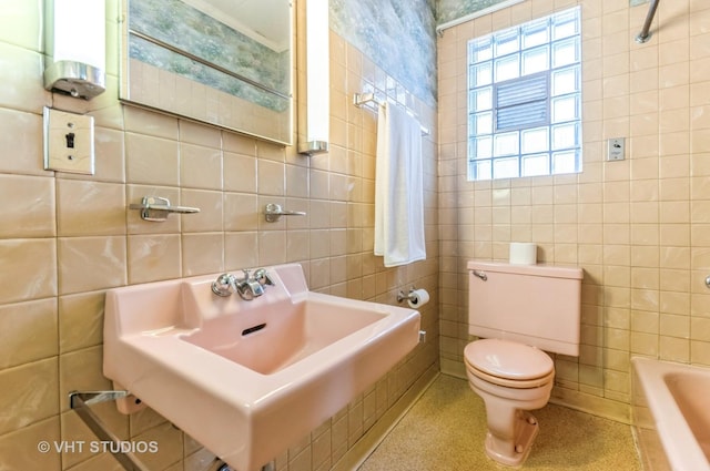 bathroom featuring a tub to relax in, tile walls, toilet, and a sink