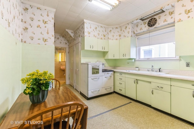 kitchen with a sink, wallpapered walls, green cabinetry, light countertops, and ornamental molding