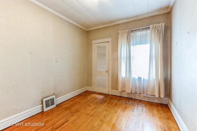 spare room with wood-type flooring, visible vents, baseboards, and ornamental molding