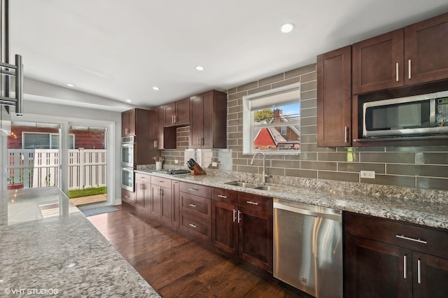 kitchen with light stone counters, a sink, stainless steel appliances, backsplash, and dark wood-style floors