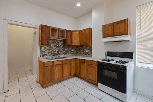 kitchen featuring under cabinet range hood, light countertops, a sink, brown cabinets, and range with gas cooktop
