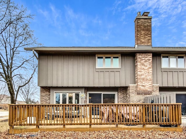 back of property featuring a chimney, brick siding, a deck, and board and batten siding
