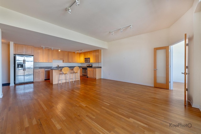 kitchen featuring open floor plan, a breakfast bar, wood finished floors, stainless steel appliances, and rail lighting
