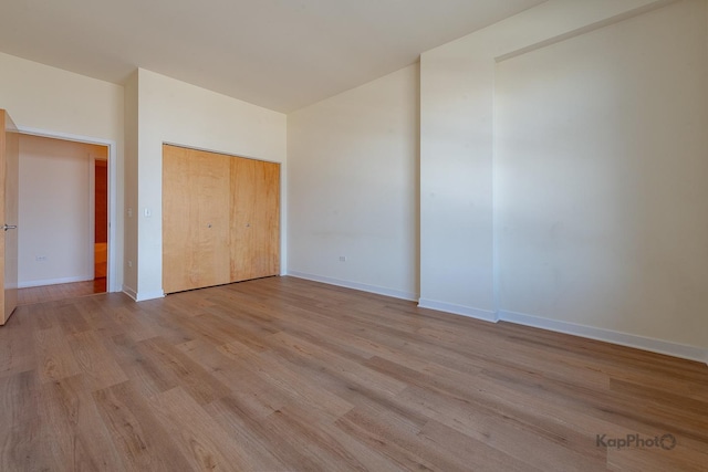 unfurnished bedroom with a closet, light wood-style floors, baseboards, and lofted ceiling