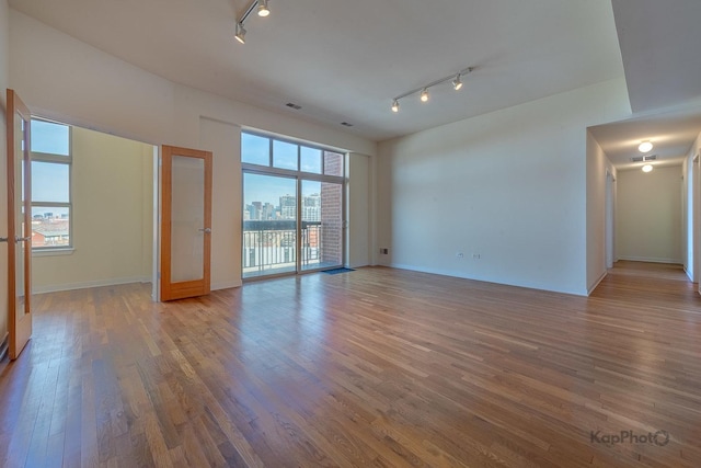 empty room with track lighting, baseboards, wood finished floors, and a city view