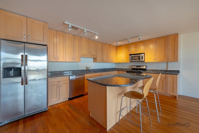 kitchen featuring a kitchen breakfast bar, a center island, appliances with stainless steel finishes, light brown cabinetry, and wood finished floors