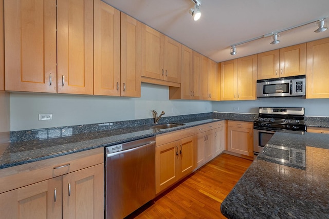 kitchen with a sink, appliances with stainless steel finishes, light wood-style floors, light brown cabinetry, and dark stone counters