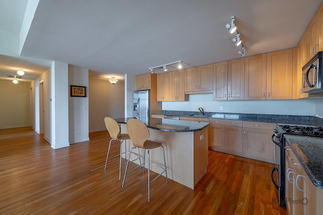 kitchen with a kitchen island, a breakfast bar area, stainless steel appliances, a sink, and wood finished floors
