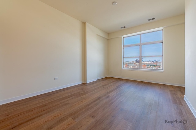 unfurnished room with wood finished floors, baseboards, and visible vents