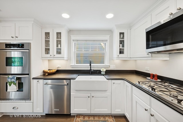 kitchen featuring glass insert cabinets, white cabinetry, appliances with stainless steel finishes, a sink, and dark countertops