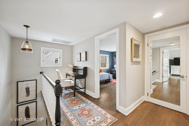hall with an upstairs landing, visible vents, baseboards, and wood finished floors