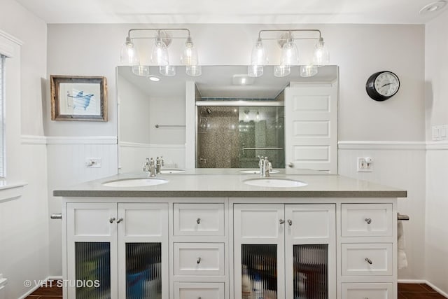 bathroom with a sink, double vanity, a stall shower, and wainscoting