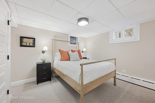 carpeted bedroom featuring a baseboard heating unit, baseboards, and a drop ceiling