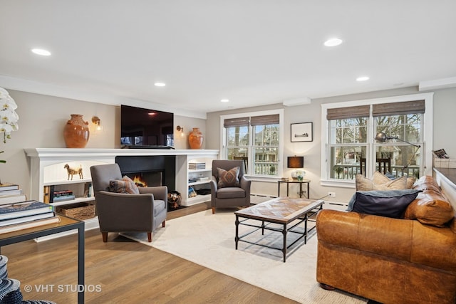 living room with a wealth of natural light, recessed lighting, a lit fireplace, and wood finished floors