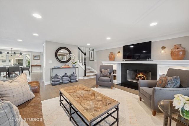 living area featuring a fireplace with flush hearth, recessed lighting, stairway, and light wood-type flooring