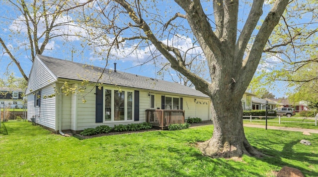 rear view of house featuring a garage, roof with shingles, fence, and a yard
