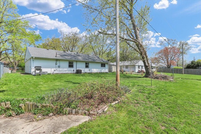 back of house with a fenced backyard, a yard, and central AC