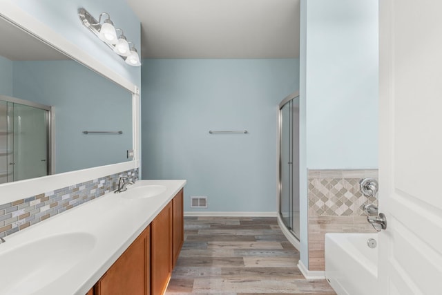 full bath featuring a sink, a shower stall, double vanity, wood finished floors, and a garden tub